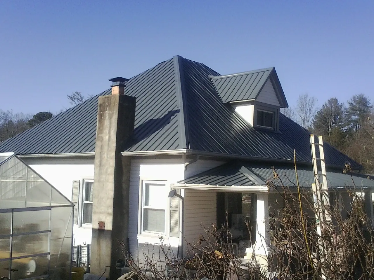 Dark blue standing seam metal roof on a white farmhouse with dormer — Slate & Tile Roof Repair by Roofing Brothers in Sweet Springs