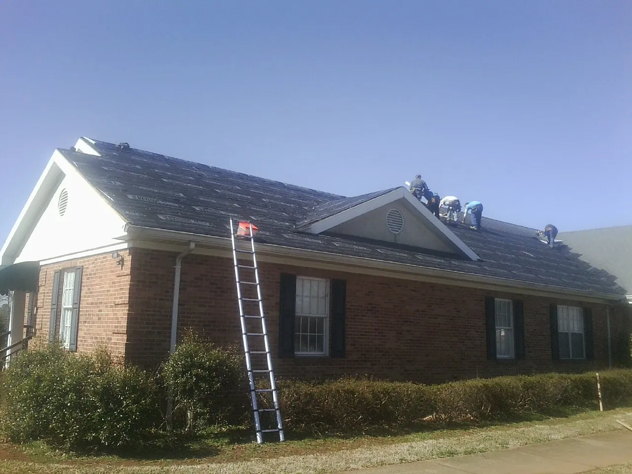 Crew tearing shingles off a brick ranch roof with a ladder set — Metal Roof Repair work by our crew in Sweet Springs