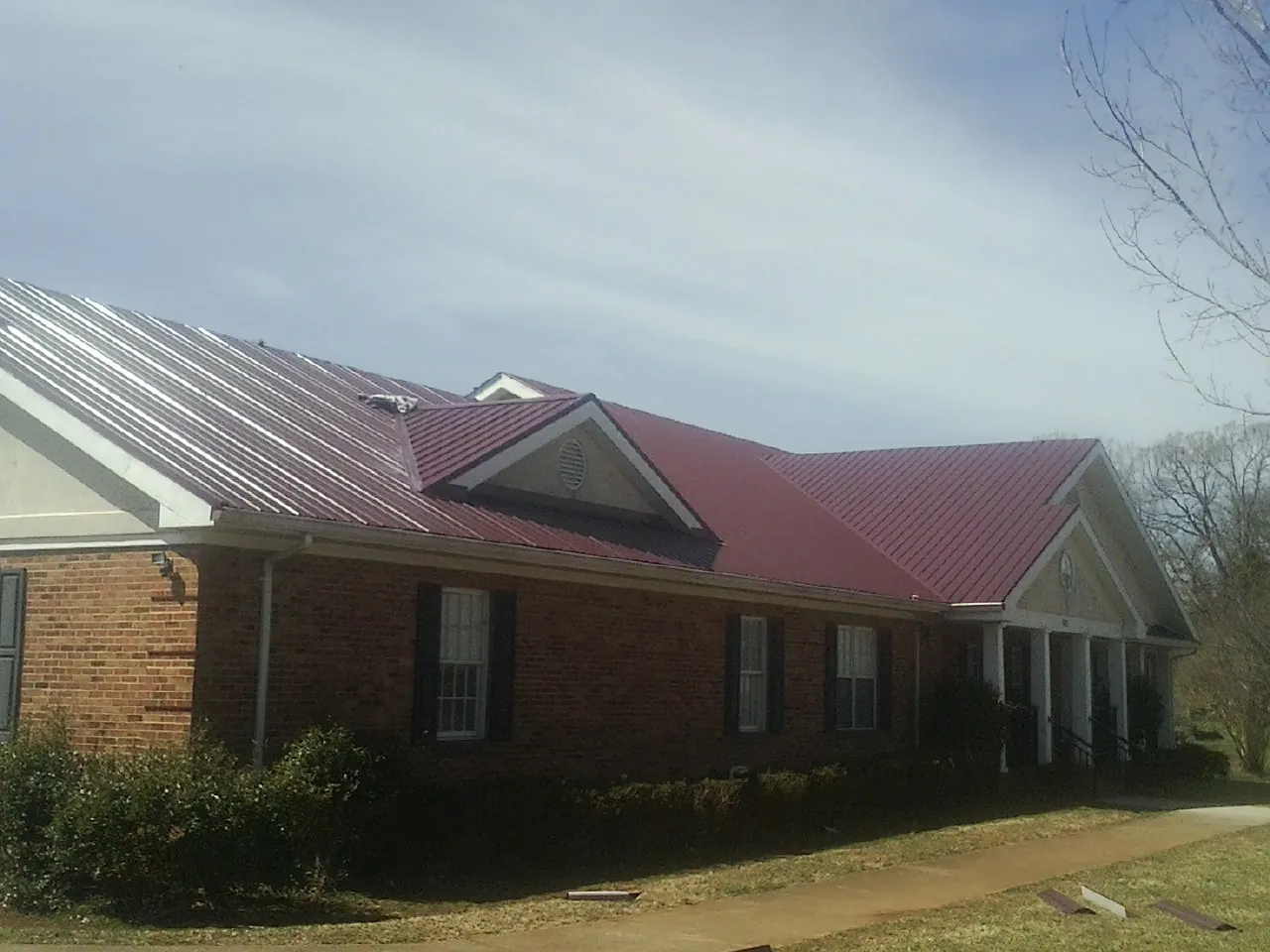 Red metal roof with gabled entries on a long brick building, from a Hail Damage Roof Repair job in Sweet Springs