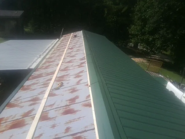 Old rusted panels beside newly installed green metal roofing — Wind Damage Roof Repair by Roofing Brothers in Sweet Springs
