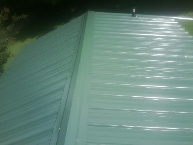New green metal panels meeting at the ridge of a roof — Flat Roof Repair work by our crew in Sweet Springs