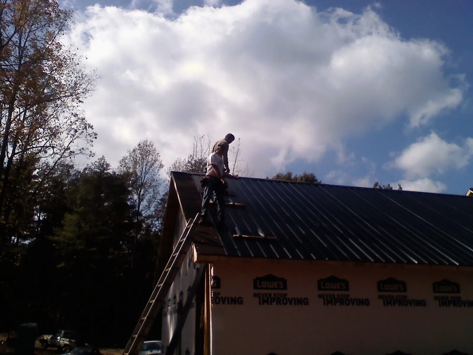 Roofer fastening dark metal panels high against a cloudy sky, from a Roof Inspection job in Sweet Springs