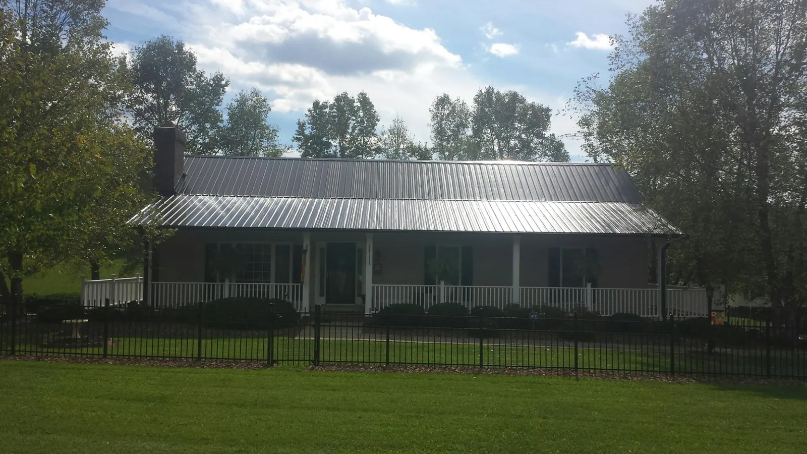 Gray metal roof on a brick ranch with a full width front porch — Gutter Guard Installation work by our crew in Sweet Springs