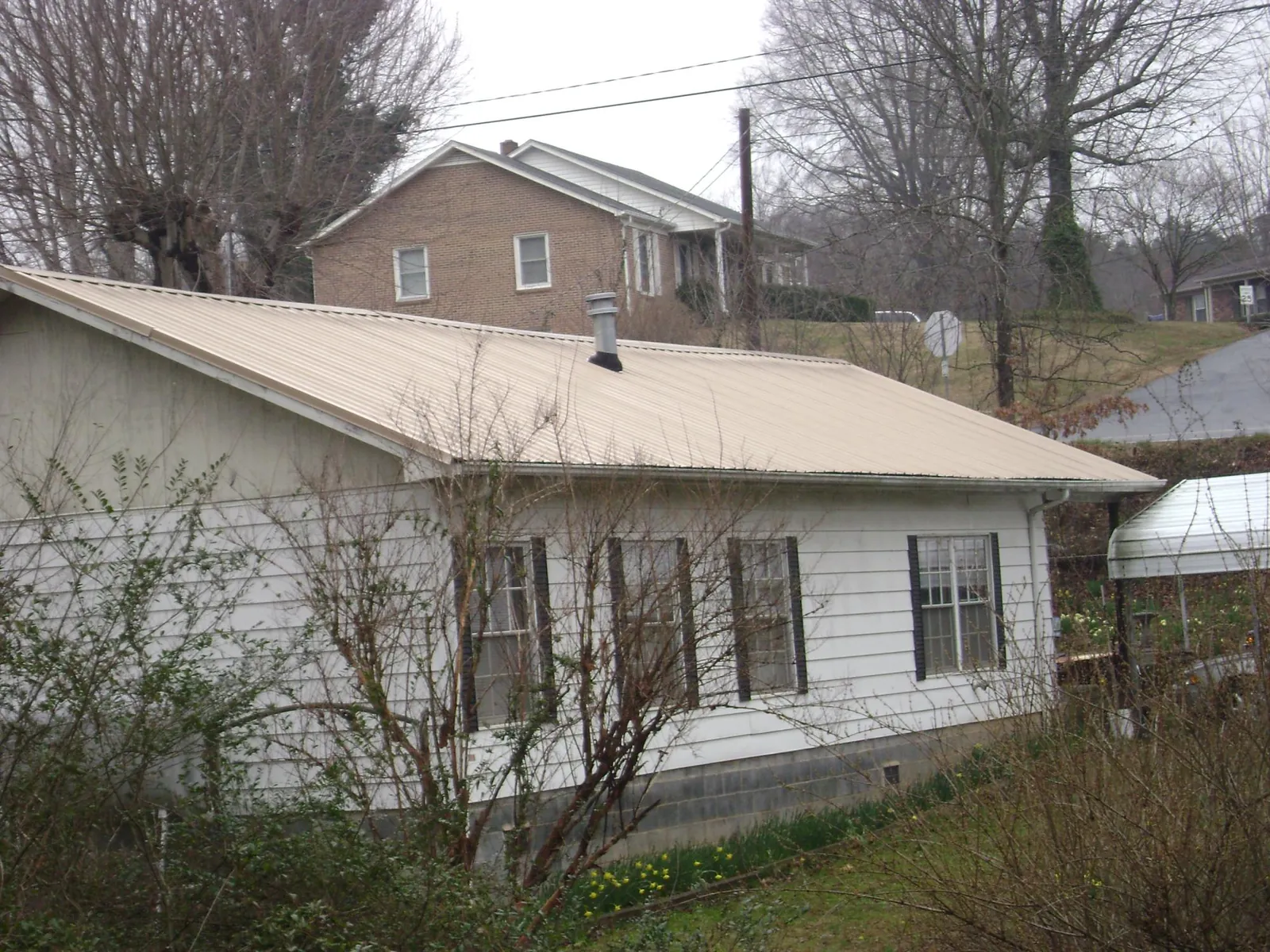 Tan metal roof on a white sided house set into a hillside — Commercial Roofing by Roofing Brothers in Sweet Springs