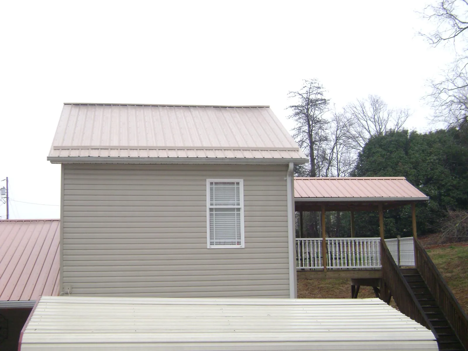 Tan metal roofs on a two story addition and attached porch, from a Roof Replacement job in Sweet Springs